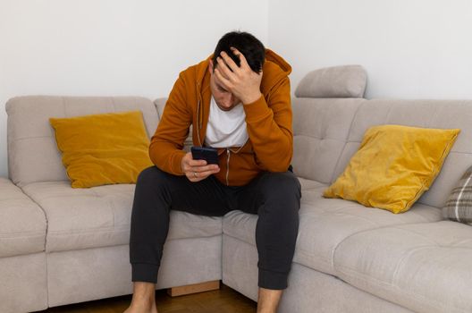 sad young man watching at mobile phone on couch. High quality photo