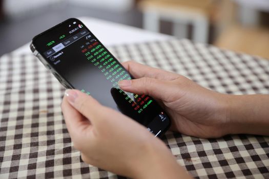 Woman hand using a smartphone for Stock exchange trading online in the coffee shop, business concept