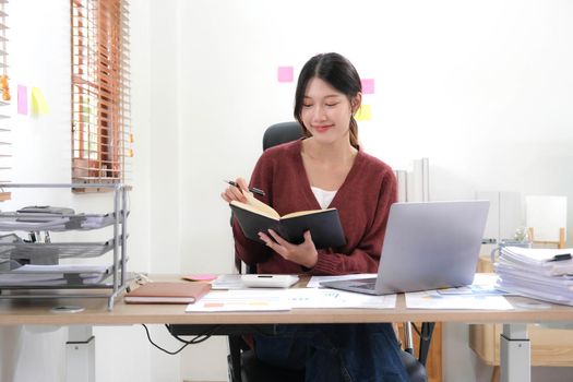 Portrait of an Asian young Female working on a laptop computer in home, Asian woman happy hold notebook and pen at home.