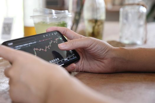 Woman hand using a smartphone for Stock exchange trading online in the coffee shop, business concept