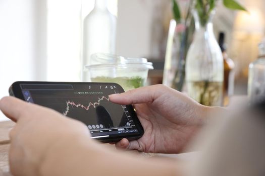 Woman hand using a smartphone for Stock exchange trading online in the coffee shop, business concept