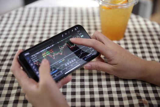 Woman hand using a smartphone for Stock exchange trading online in the coffee shop, business concept