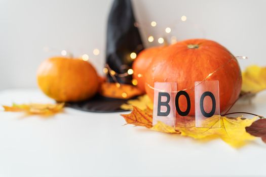 Autumn leaves with pumpkin border at the bottom, black hat, beautiful autumn background. Flashing lights in the background, beautiful bokeh. The inscription boo on the background of the pumpkin