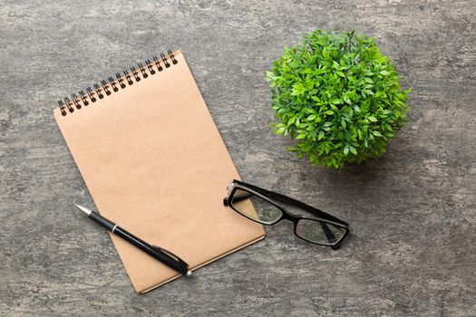 Modern office desk table with notebook and other supplies with green tree. Blank notebook page for you design. Top view, flat lay.