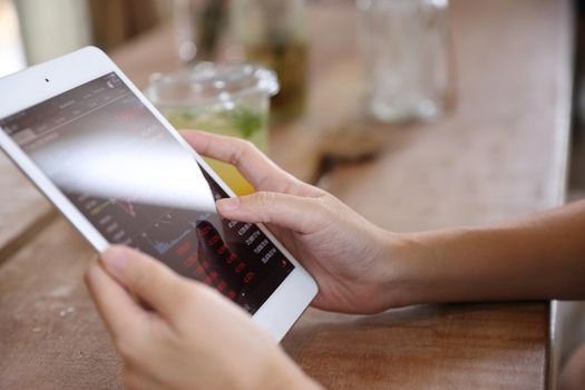 Woman hand using a tablet for Stock exchange trading online in the coffee shop, business concept