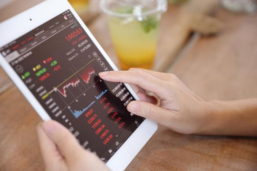 Woman hand using a tablet for Stock exchange trading online in the coffee shop, business concept