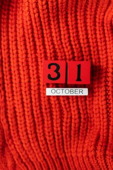 Wooden cube calendar showing October 31, Halloween isolated on red background red knitted sweater