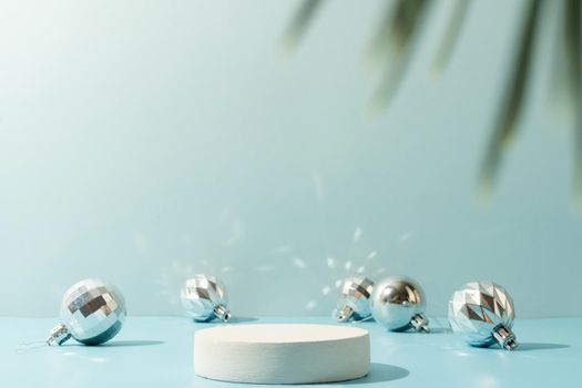 A minimalistic scene of a podium with christmas decorative balls and pine tree on a light blue background. Catwalk for the presentation of products and cosmetics. Showcase with a stage for products, mockup design, seasonal