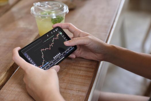 Woman hand using a smartphone for Stock exchange trading online in the coffee shop, business concept