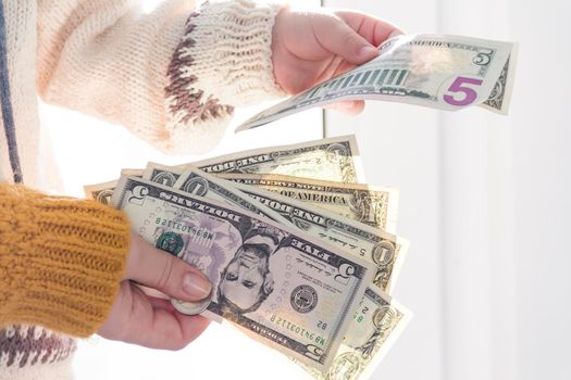 Women's hands and children's hands in a yellow sweater hold small dollar bills..