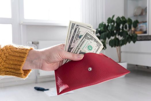 Women's hands in a yellow sweater are holding an open, red purse with money..