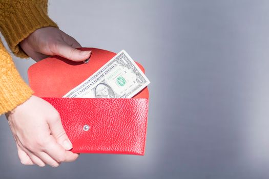 Women's hands in a yellow sweater are holding an open, red purse with money..