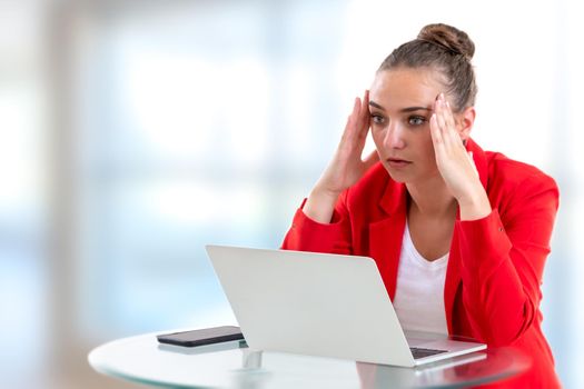 Woman facing her computer squeezing her head with her fingers.