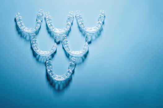 invisible plastic braces lie in a pyramid shape in a row on a blue background, studio shot, nobody.