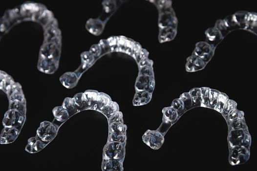 Close-up, invisible aligners on a black background in the form of a pattern. Plastic braces for teeth alignment.