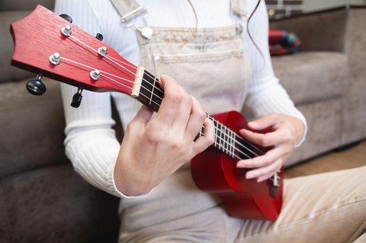 close-up, ukulele in female hands, hipster learns to play a musical instrument at home, sitting on the floor near the sofa.