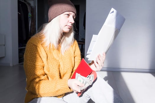 A young girl in a yellow sweater and hat is studying large bills, taxes and utility bills..