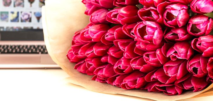 a bouquet of flowers on the table against the backdrop of a laptop. The concept of ordering flowers online, buying flowers in online stores. Buying and selling tulips , online order