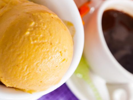 Scoop of gourmet pumpkin gelato in white bowl with cup of coffee.