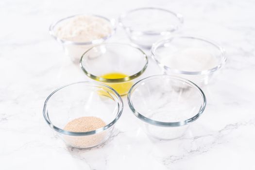 Measured ingredients in a glass mixing bowl to prepare pizza dough.