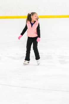 Little girl practicing figure skating moves on the indoor ice rink.