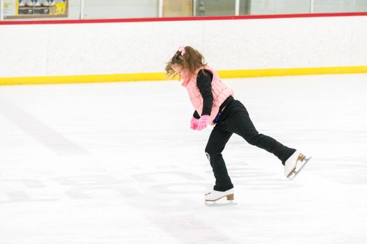 Little girl practicing figure skating moves on the indoor ice rink.