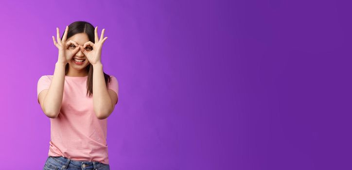 Cheerful friendly carefree asian woman having fun fool around, show okay ok signs on eyes make glasses from fingers, smiling delighted, mimicking funny emotions, stand purple background happy.