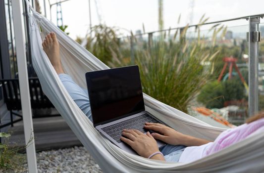 young woman freelancer working in hammock on the terrace. High quality photo