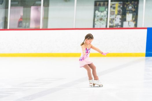 Little girl practicing figure skating on an indoor ice skating rink.