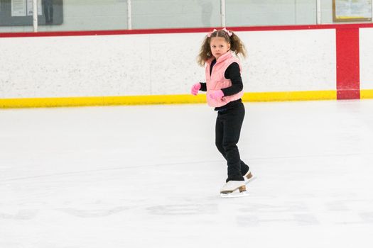 Little girl practicing figure skating moves on the indoor ice rink.