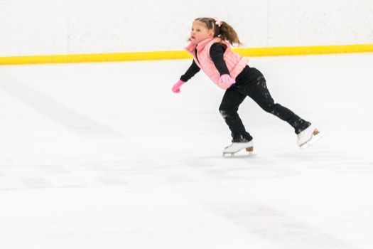 Little girl practicing figure skating moves on the indoor ice rink.