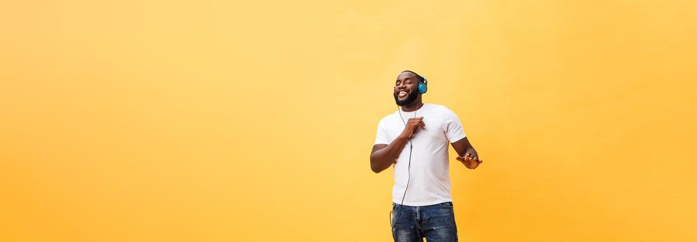 Full length portrait of a cherry young african american man listening to music with headphones and dancing isolated over yellow background.