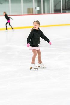 Little girl practicing figure skating on an indoor ice skating rink.