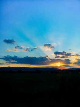 Beautiful shining sun behind big clouds at sunset over big fields