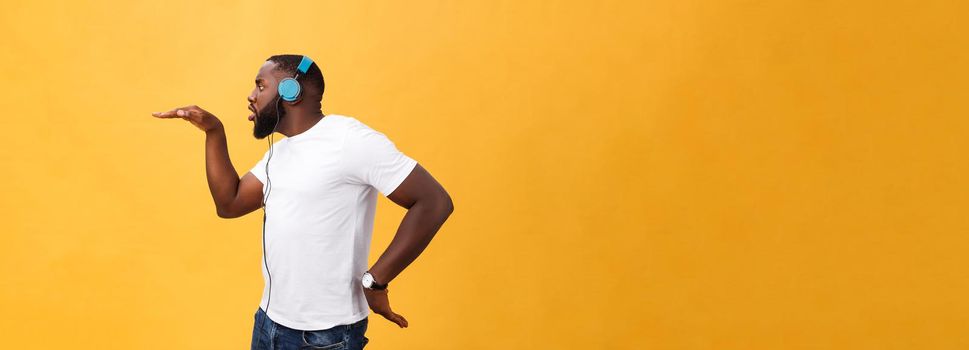 Young African American man wearing headphone and enjoy music dancing over yellow gold Background.