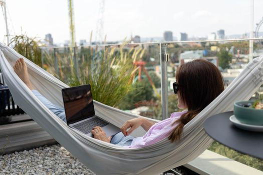 young woman freelancer working in hammock on the terrace. High quality photo