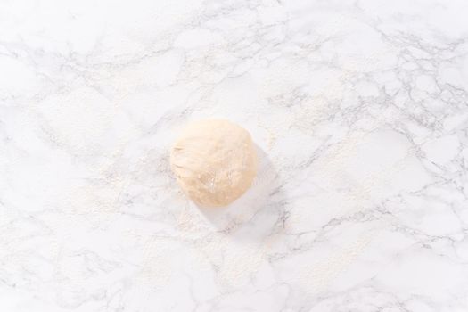 Flat lay. Rolling pizza dough with a french rolling pin to prepare cinnamon dessert pizza.