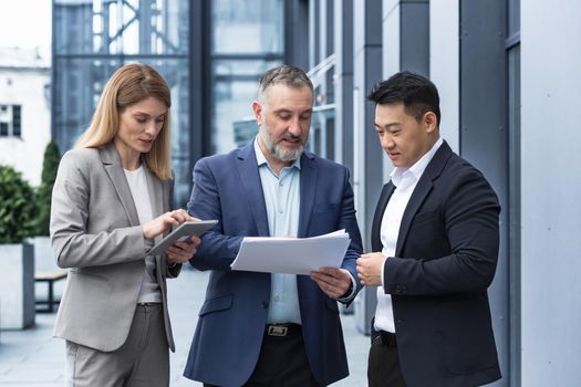 International business team meeting mature man, Caucasian woman, Asian employee communicate . group of entrepreneurs in formal suits discuss a project document near office center on street