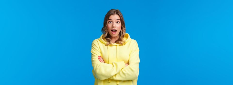 Really omg. Impressed and surprised blond woman react astonished listening stunning shocking story, open mouth and look camera with amazement, cross hands chest casual pose over blue background.