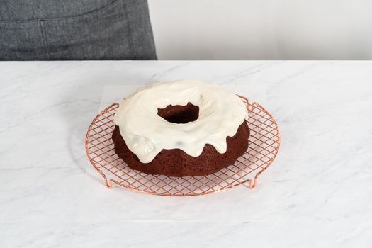 Pouring cream cheese glaze over freshly baked red velvet bundt cake.