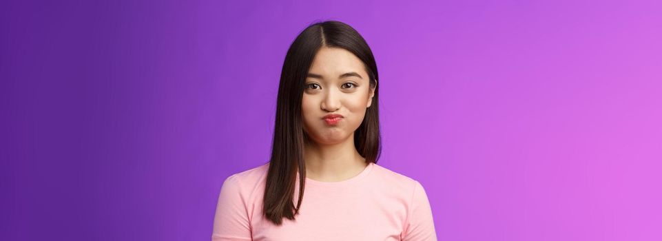 Close-up cute tender young asian female holding breath speechless, smiling silly having challenge hiding secret unwilling talk, pouting lovely, look camera entertained, purple background.