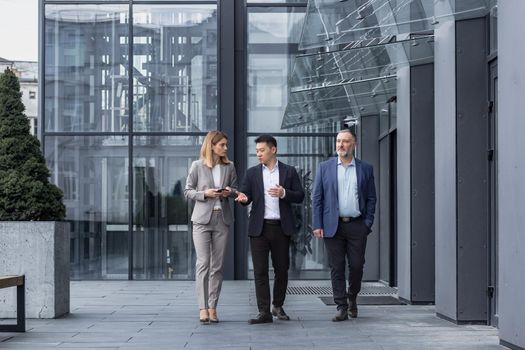 Three diverse business people walking and talking focused and thoughtful seriously outside office building, male and female, discussing plans and work project