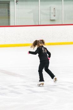 Little girl practicing figure skating moves on the indoor ice rink.