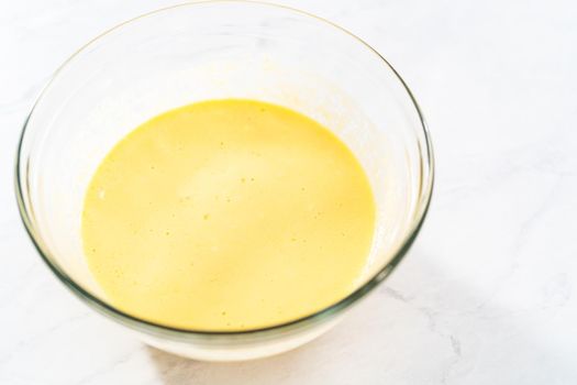 Mixing ingredients in a large glass mixing bowl to bake red velvet bundt cake with cream cheese glaze.