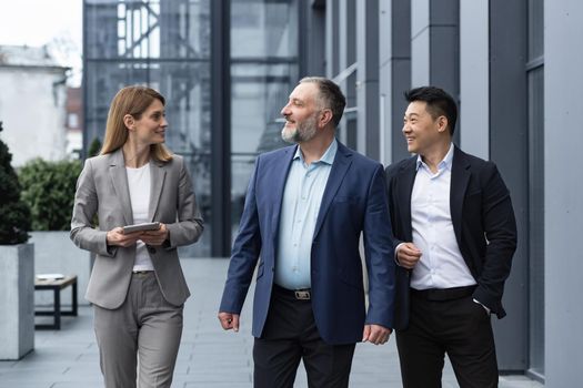 A diverse team of IT specialists, senior and experienced engineers managers team leaders, a group of three workers happily strolling outside an office building, colleagues in business suits.
