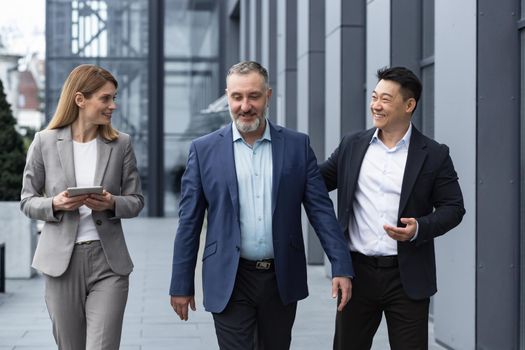A diverse team of IT specialists, senior and experienced engineers managers team leaders, a group of three workers happily strolling outside an office building, colleagues in business suits.