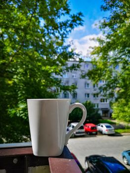 White cup of coffee standing on edge of balcony railing