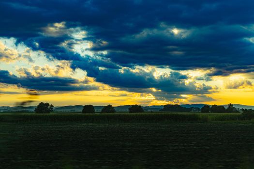 Beautiful shining sun behind big clouds at sunset over big fields