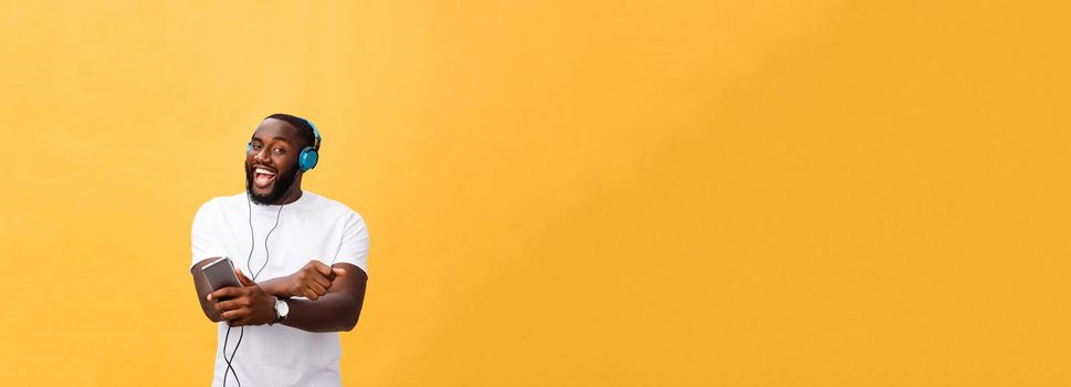 African American man with headphones listen and dance with music. Isolated on yellow background.