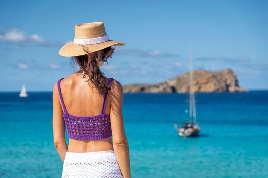 Brunette woman with hat, white skirt and purple top on the shore of the Mediterranean